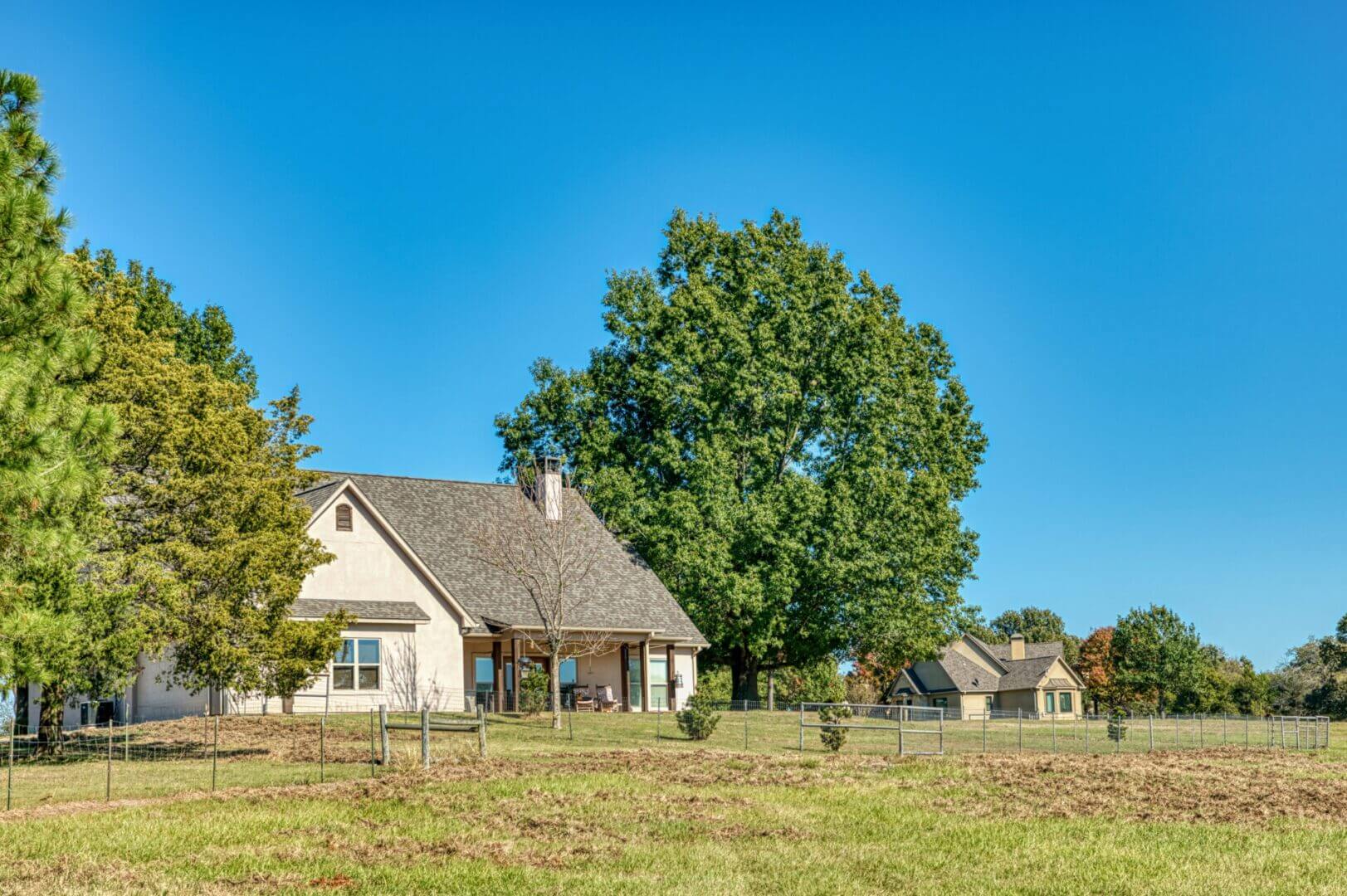 A peaceful rural scene with houses and large trees under a clear blue sky.